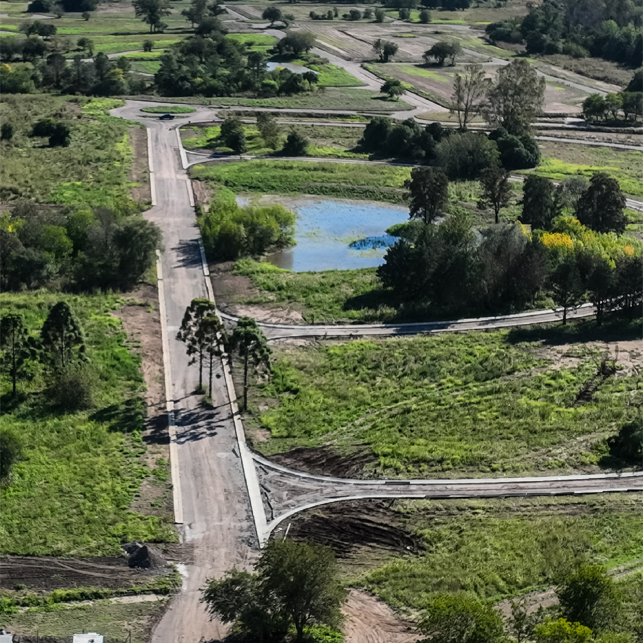 Vista aérea de calles internas en construcción en Viarava, con trazado curvo, vegetación natural y laguna integrada al paisaje.